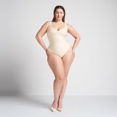 SKIMS BODY UNLINED PLUNGE THONG BODYSUIT | SAND ON A MODEL FRONT VIEW @