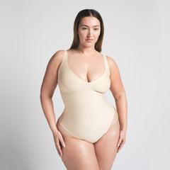 SKIMS BODY UNLINED PLUNGE THONG BODYSUIT | SAND ON A MODEL FRONT VIEW @