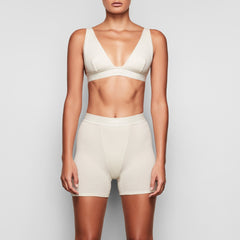 A MODEL STANDS FACING FORWARD WEARING THE SKIMS COTTON RIB BOXER IN BONE