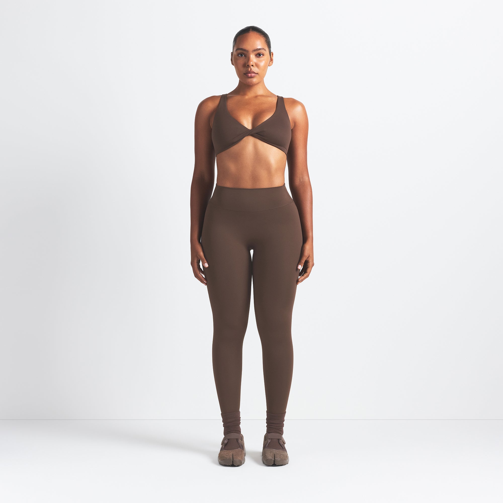 NikeSKIMS MATTE TWIST-FRONT BRA | DARK SEPIA ON A MODEL FRONT VIEW @ | FOCUS: 0.0, 1.0, 0.9