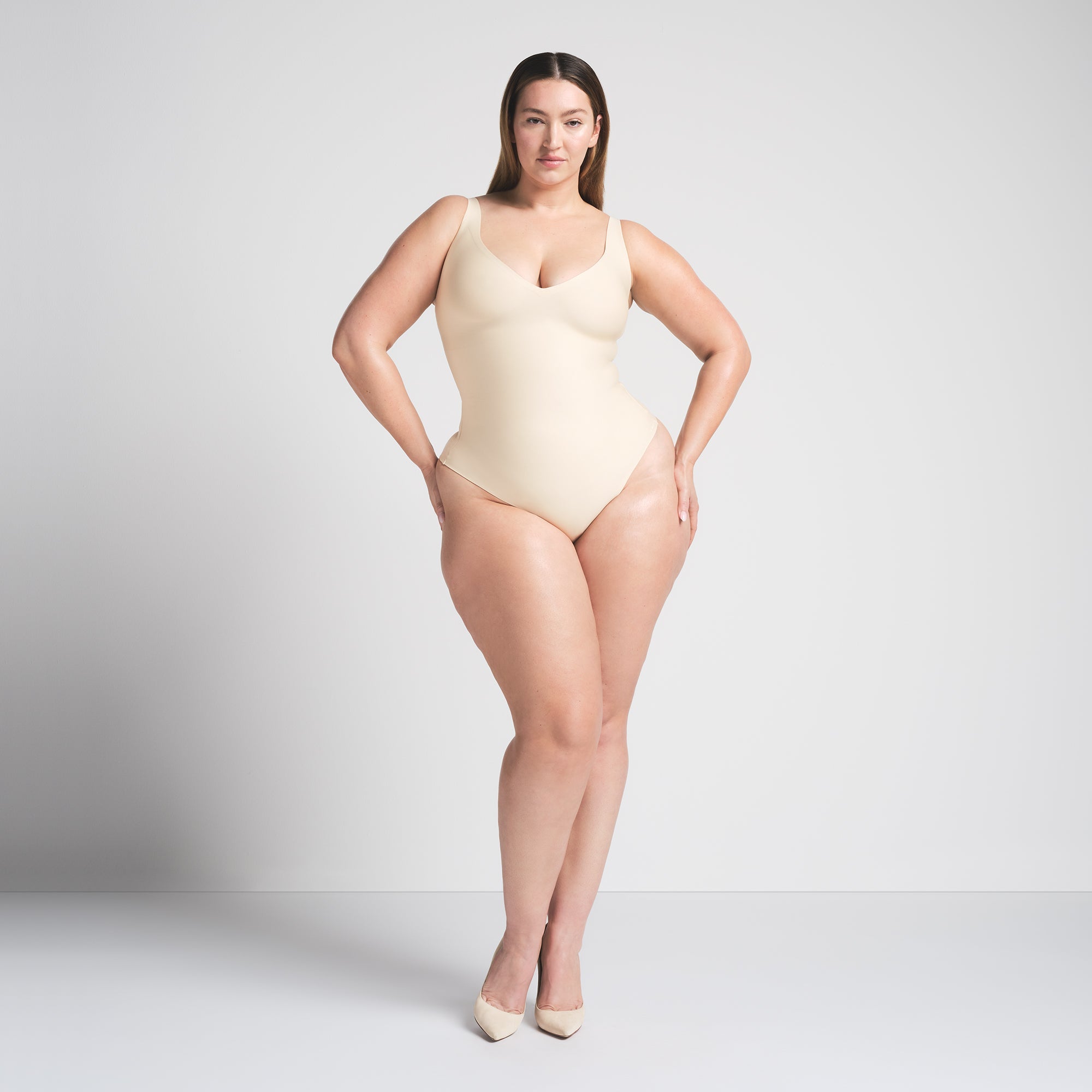 SKIMS BODY UNLINED PLUNGE THONG BODYSUIT | SAND ON A MODEL FRONT VIEW @