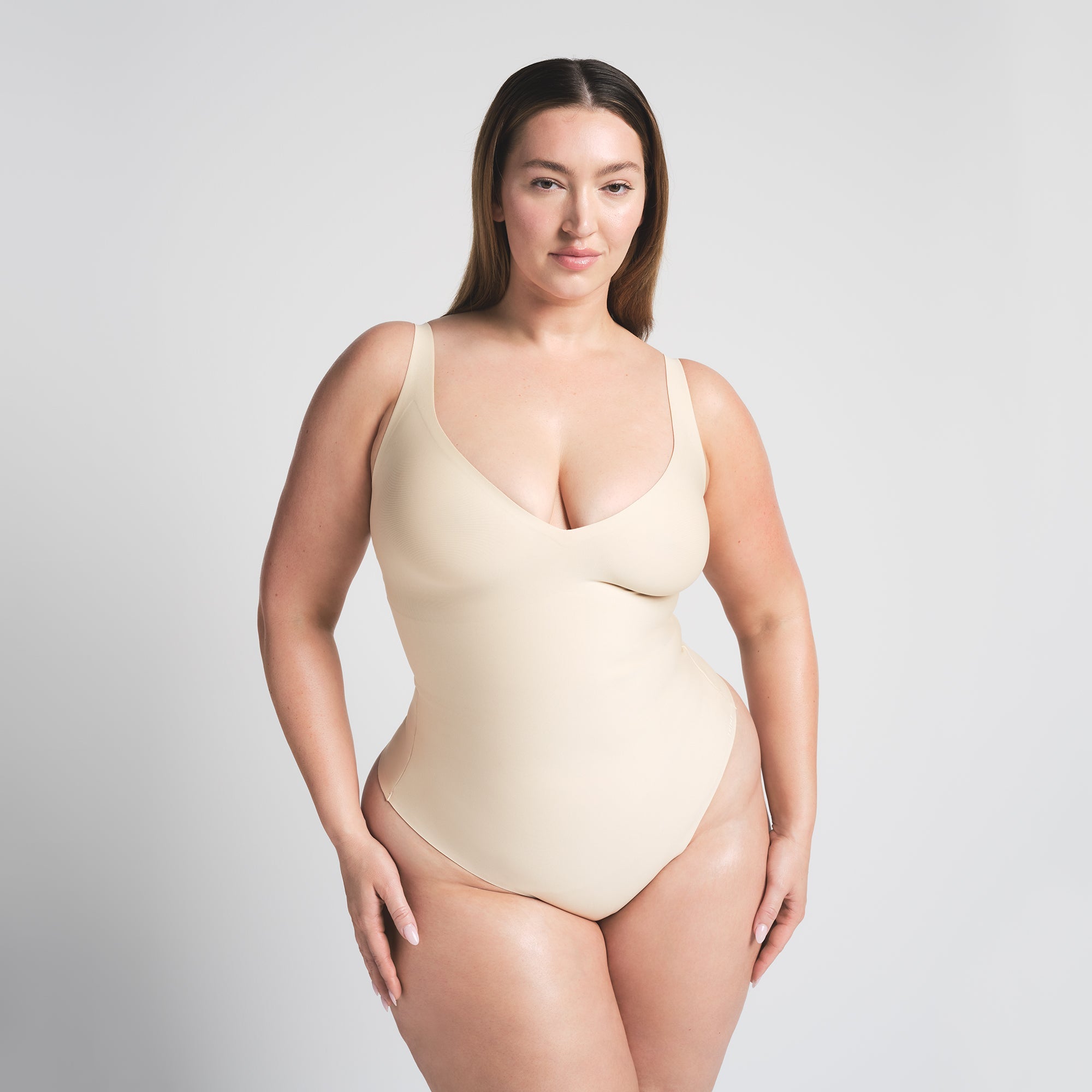 SKIMS BODY UNLINED PLUNGE THONG BODYSUIT | SAND ON A MODEL FRONT VIEW @