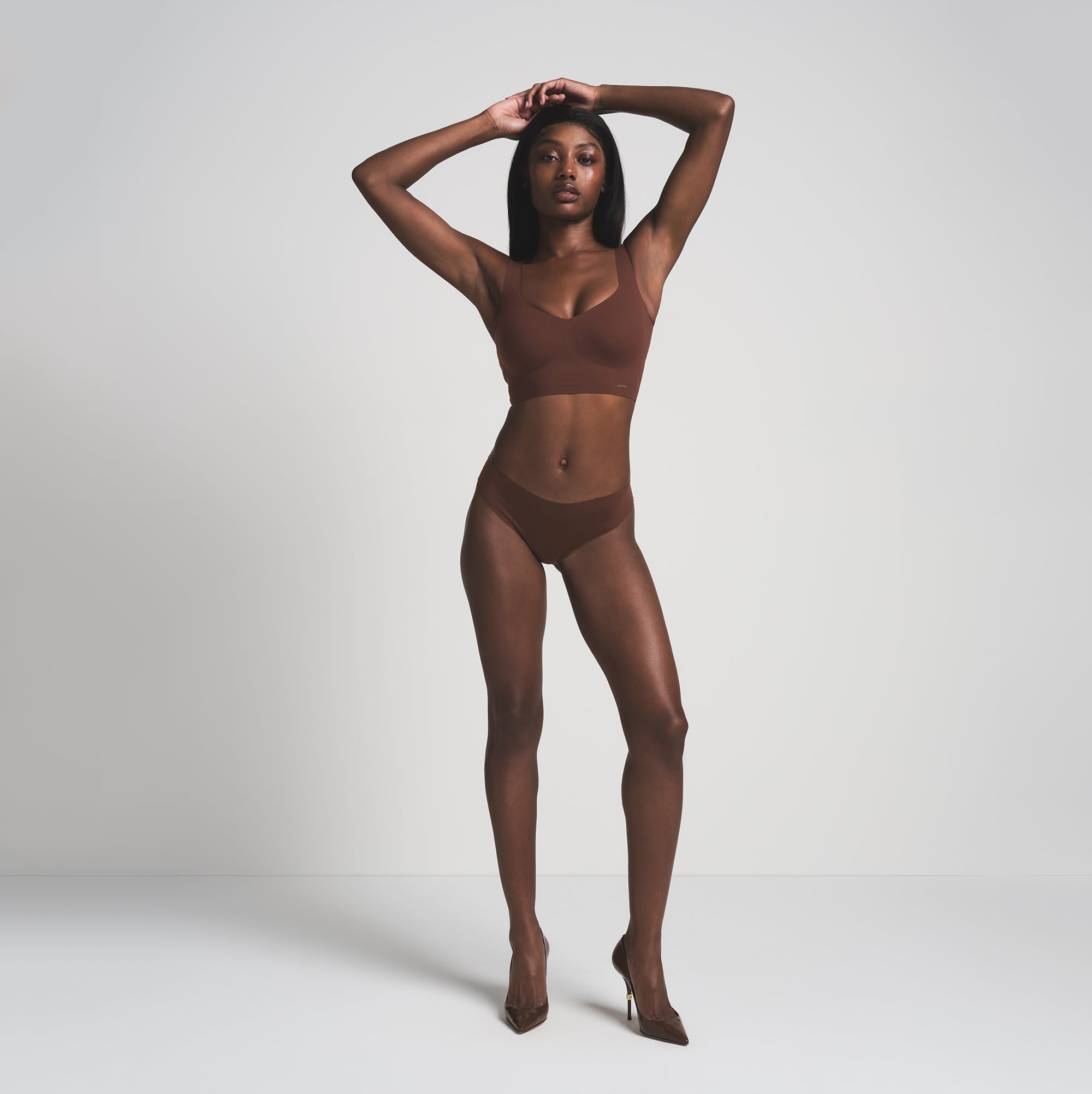 A MODEL STANDS FACING FORWARD WEARING THE SKIMS FREE CUT MID WAIST TANGA IN COCOA  | FOCUS: 0.0, 1.0, 0.9