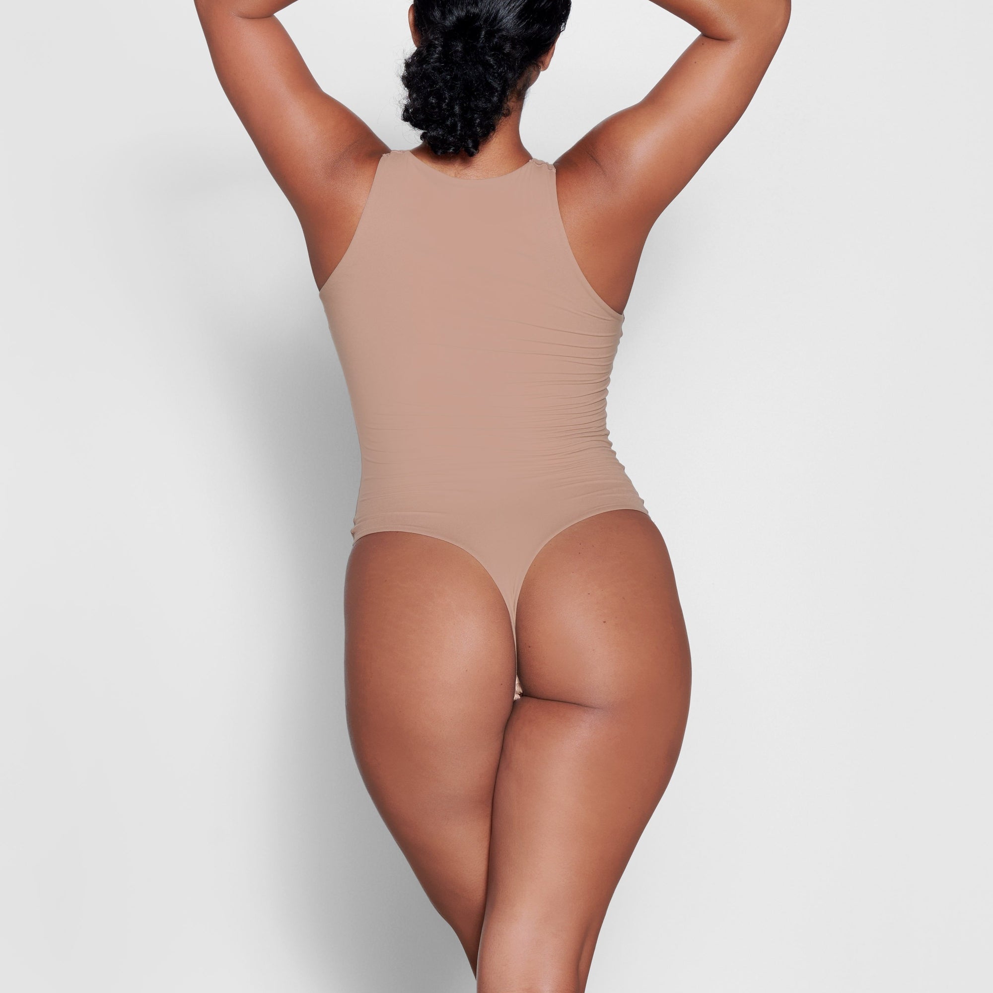 A MODEL STANDS WITH HER BACK TO THE CAMERA SHOWING THE FITS EVERYBODY HIGH NECK BODYSUIT | SIENNA