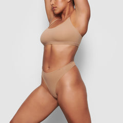 A MODEL STANDS SIDEWAYS SHOWING THE PROFILE OF THE FITS EVERYBODY SCOOP NECK BRA | SIENNA