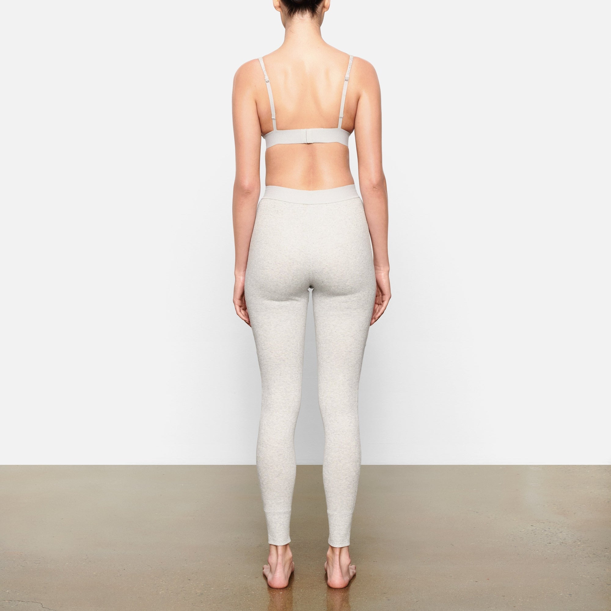 A MODEL STANDS WITH HER BACK TO THE CAMERA SHOWING THE COTTON RIB LEGGING | LIGHT HEATHER GREY