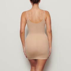 A MODEL STANDS WITH HER BACK TO THE CAMERA SHOWING THE FITS EVERYBODY SLIP DRESS | CLAY